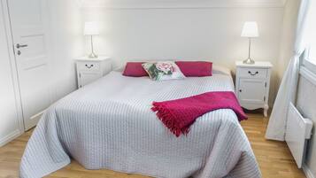 A bedroom with a bed, two bedside tables, a lamp on each, a radiator, and a door.