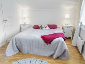 A bedroom with a bed, two bedside tables, a lamp on each, a radiator, and a door.