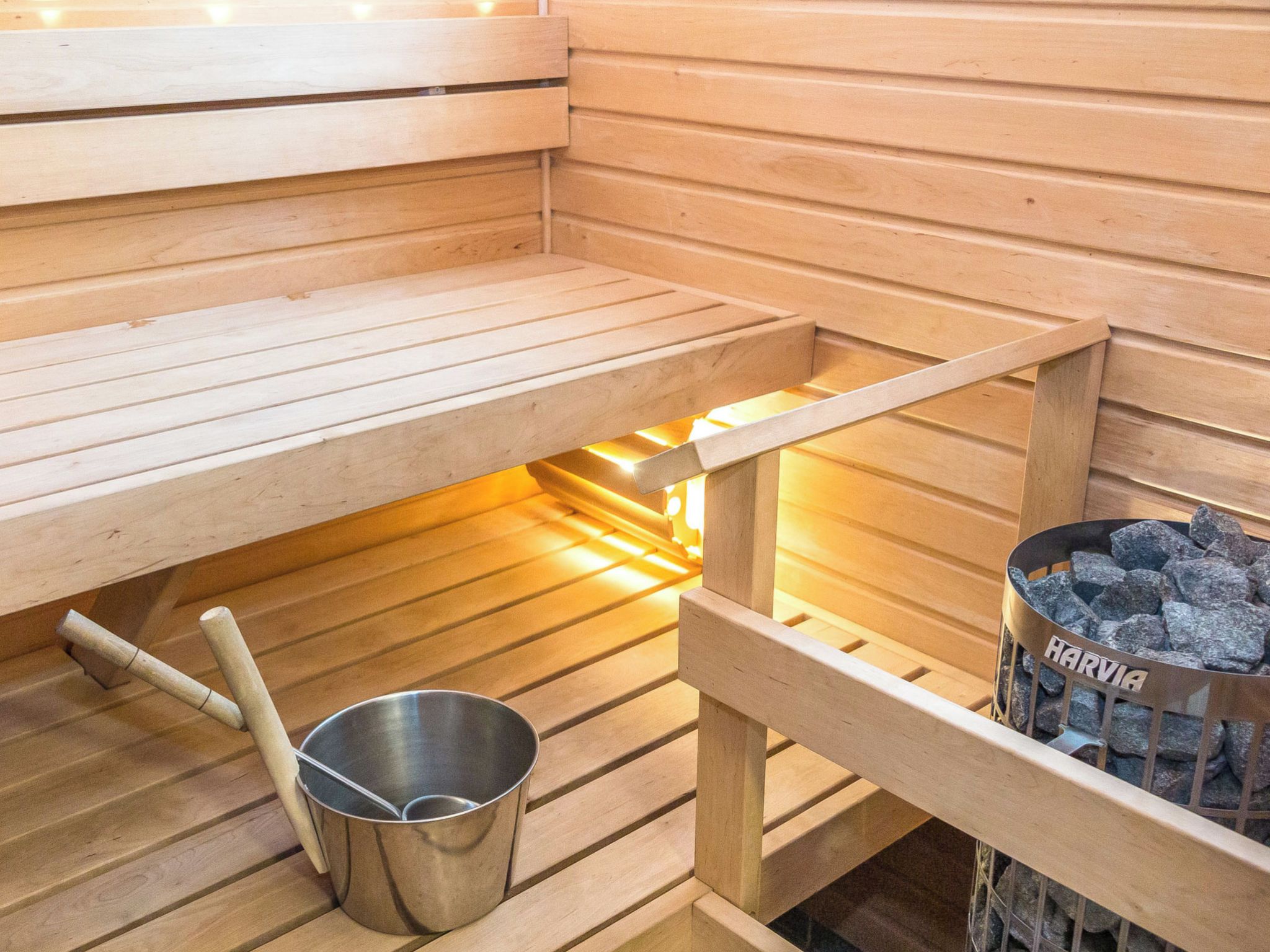 A sauna room with wooden benches, a metal bucket, and a charcoal container labeled 'HARVIA'.