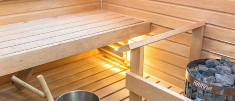 Ein Saunaraum mit Holzbänken, einem Metallkübel und einem Behälter für Holzkohle mit dem Aufdruck 'HARVIA'.
