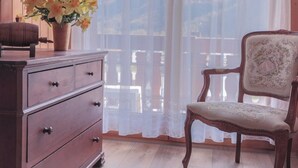 Une commode en bois avec des tiroirs, un vase rempli de fleurs jaunes et un fauteuil ancien orné d’un motif floral.
