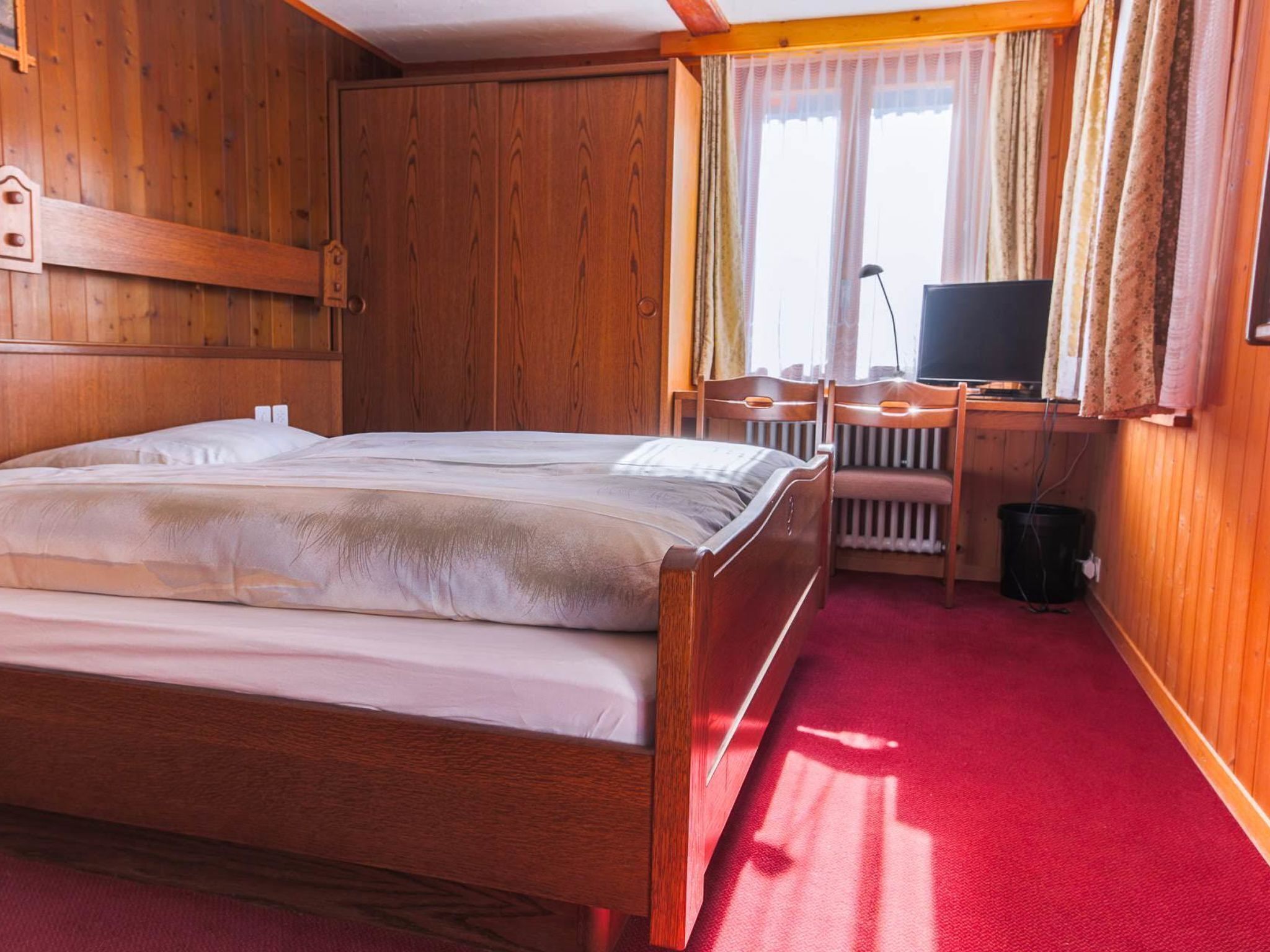 A wooden room with a bed, a desk, a chair, and a television.