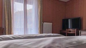 Une chambre d’hôtel avec un lit, une télévision, une chaise et une fenêtre avec des rideaux.