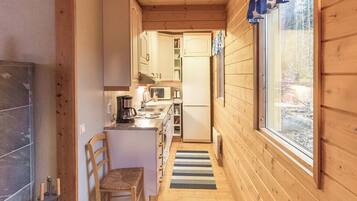Un intérieur étroit en bois, comprenant un coin cuisine, une table à manger et une fenêtre avec des rideaux.