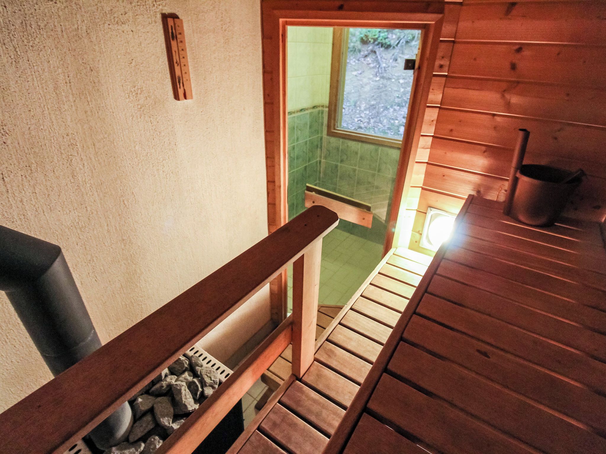 Een houten trap leidt naar een badkamer met een groen betegelde muur en een raam.