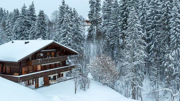 Eine Holzhütte mit Balkon, umgeben von schneebedeckten Bäumen.