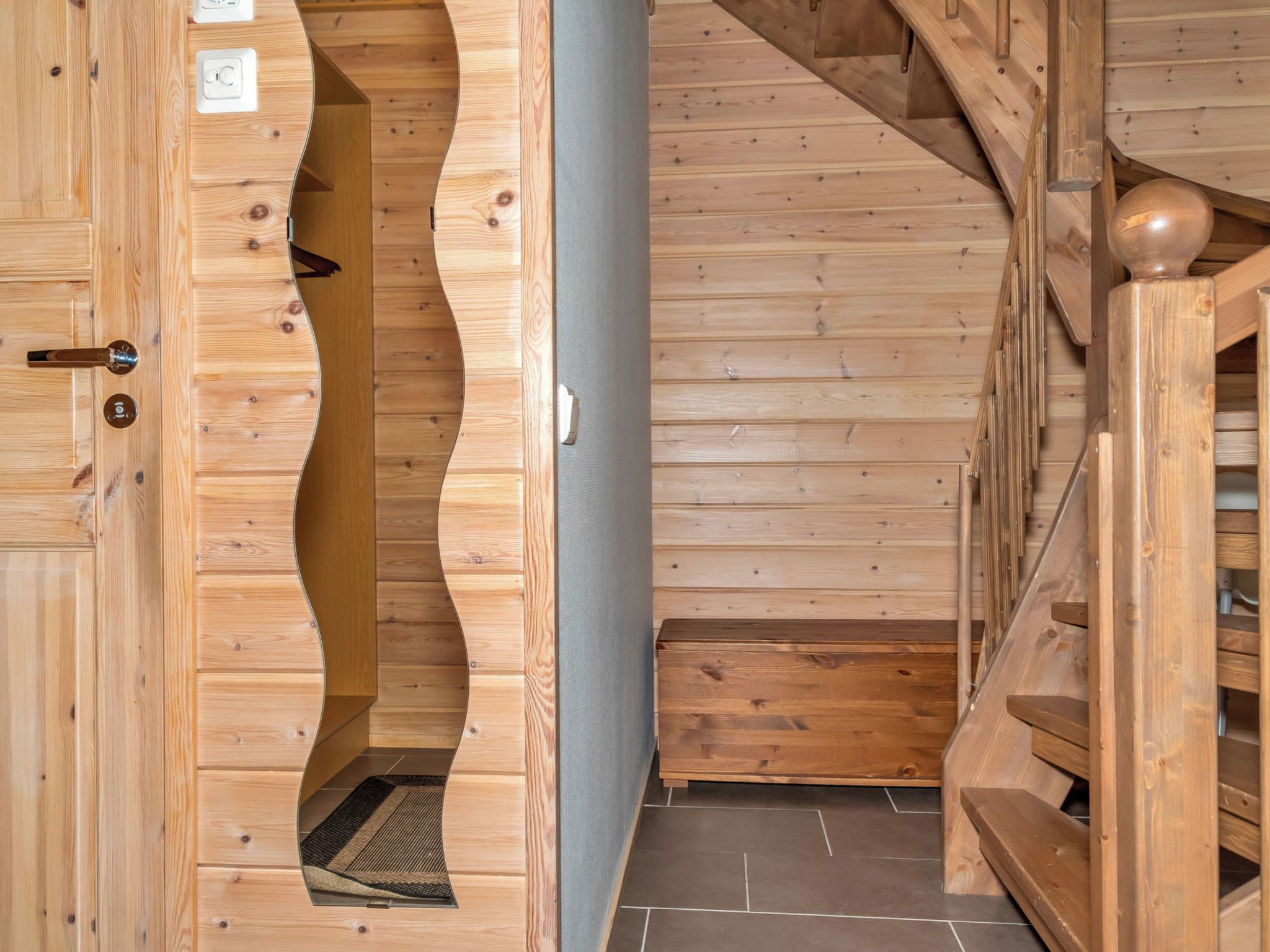 Ein Holzinnenraum mit einer gewölbten Tür, einer Treppe und einem Fliesenboden.