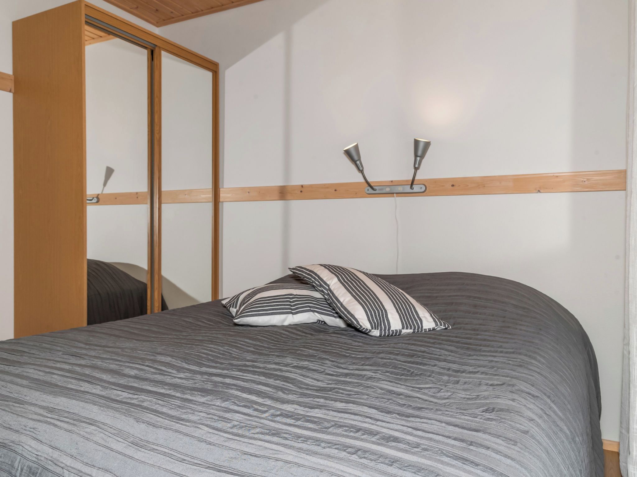 Une chambre à coucher avec un lit, une tête de lit en bois, un miroir et un luminaire fixé au mur.