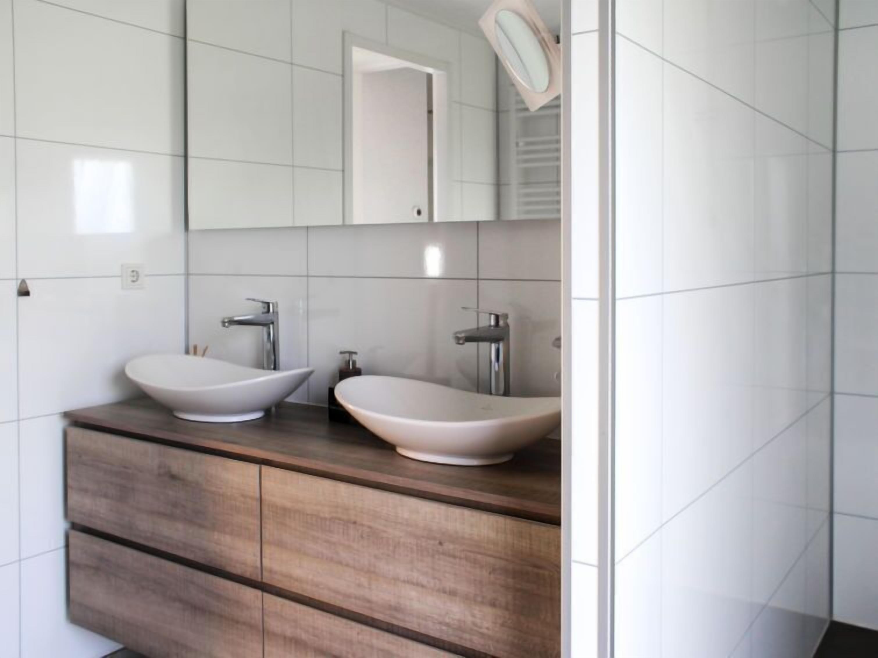 A modern bathroom with two vessel sinks, a large mirror, and a wooden vanity.