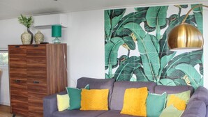 A modern living room with a grey sofa, yellow and green cushions, a wooden coffee table, and a large tropical leaf wallpaper. - Ravenbosch+ 5p by Interhome (Bemelen)