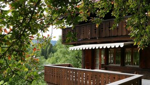 Een houten gebouw met een balkon, omgeven door weelderige begroeiing en bergen op de achtergrond.