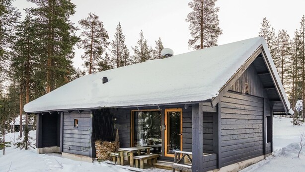 Une cabane dotée d’un porche abrité, d’une façade en bois et d’un toit recouvert de neige.