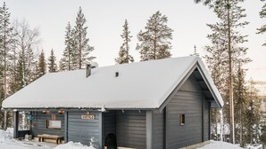Une cabane en bois dont le toit est recouvert de neige, avec un banc en bois à l’extérieur et une enseigne sur laquelle on peut lire « KARPALO ».