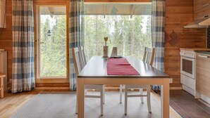 L’intérieur d’un chalet en bois comprend une table à manger, des chaises, un set de table rouge et un coin cuisine avec un poêle.
