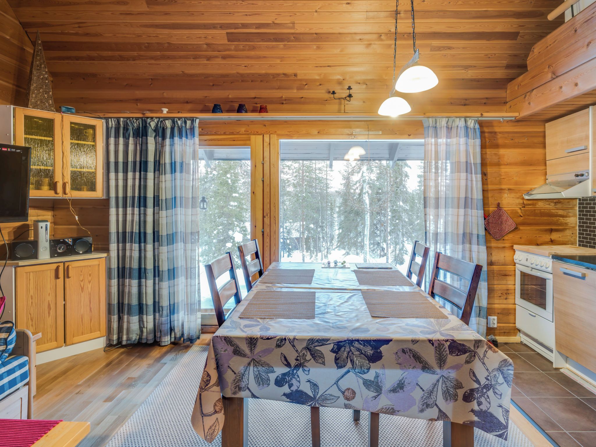 A wooden interior with a dining table, chairs, a kitchen area, and a television.