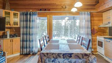 A wooden interior with a dining table, chairs, a kitchen area, and a television.