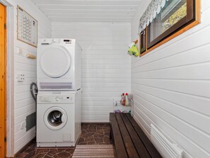 A laundry room with stacked washers and dryers, a bench, and a small shelf with cleaning supplies. - Lomaranta by Interhome (Polvijärvi)