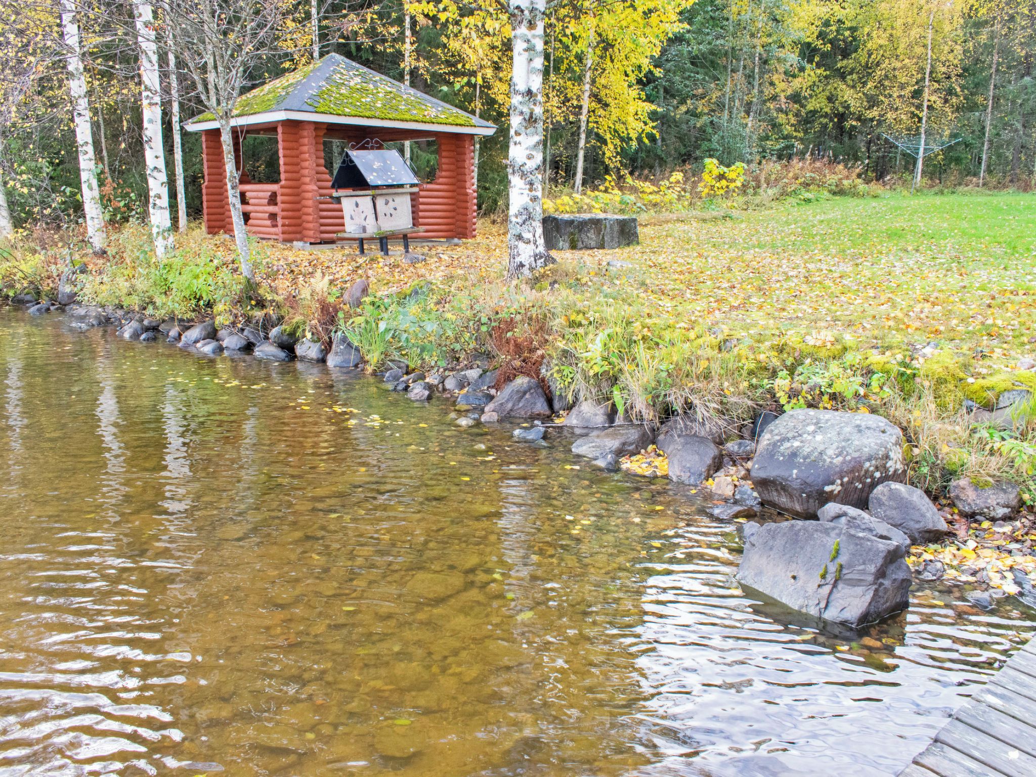 Une cabane au bord d’un ruisseau aux eaux limpides, avec un quai en bois.