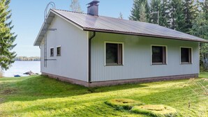 Ett envåningshus med ett tak av metall, en skorsten och en liten veranda. Huset omges av en välskött gräsmatta och träd.