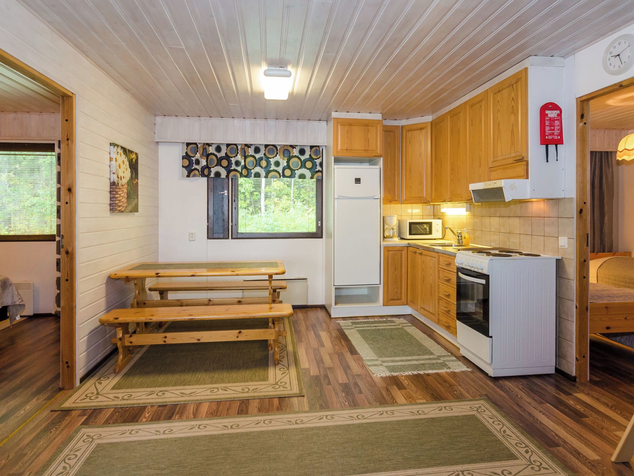 Une cuisine compacte avec des meubles en bois, un four à micro-ondes, une cuisinière et un réfrigérateur. On y trouve également un banc et une fenêtre donnant sur un paysage verdoyant.