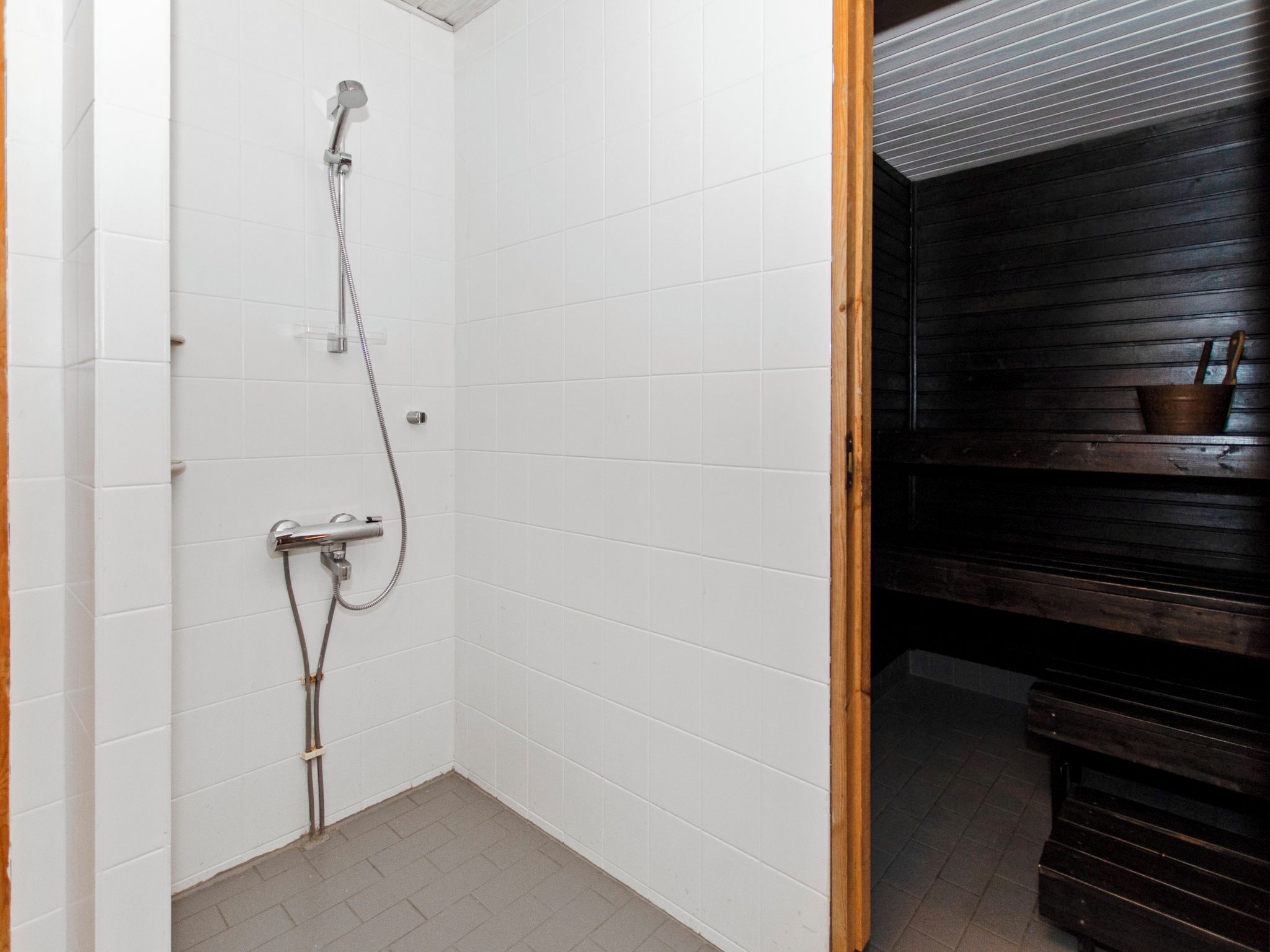 A small, tiled bathroom with a shower, a wooden bench, and a dark wooden wall.