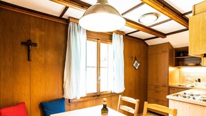 A cozy room with wooden walls, a dining table with chairs, a cross on the wall, and a window with curtains. - Bürcher Haus 2. OG Süd by Interhome (Riederalp)