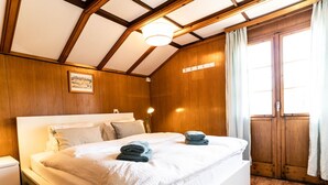 A bedroom with a large bed, wooden walls, a wooden ceiling, a bedside table, and a window with curtains. - Bürcher Haus 2. OG Süd by Interhome (Riederalp)