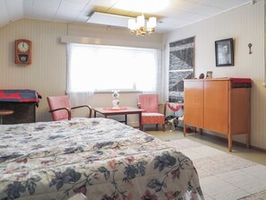 Une chambre à coucher avec un lit, deux chaises, une petite table, une armoire, une horloge et une fenêtre.