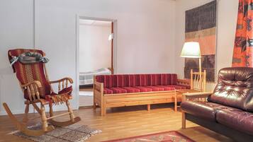 A living room with a wooden floor, a red sofa, a leather armchair, a rocking chair, a lamp, and a patterned rug.