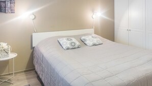 A neatly made bed with a quilted headboard, two patterned pillows, and a bedside table with a white lamp.