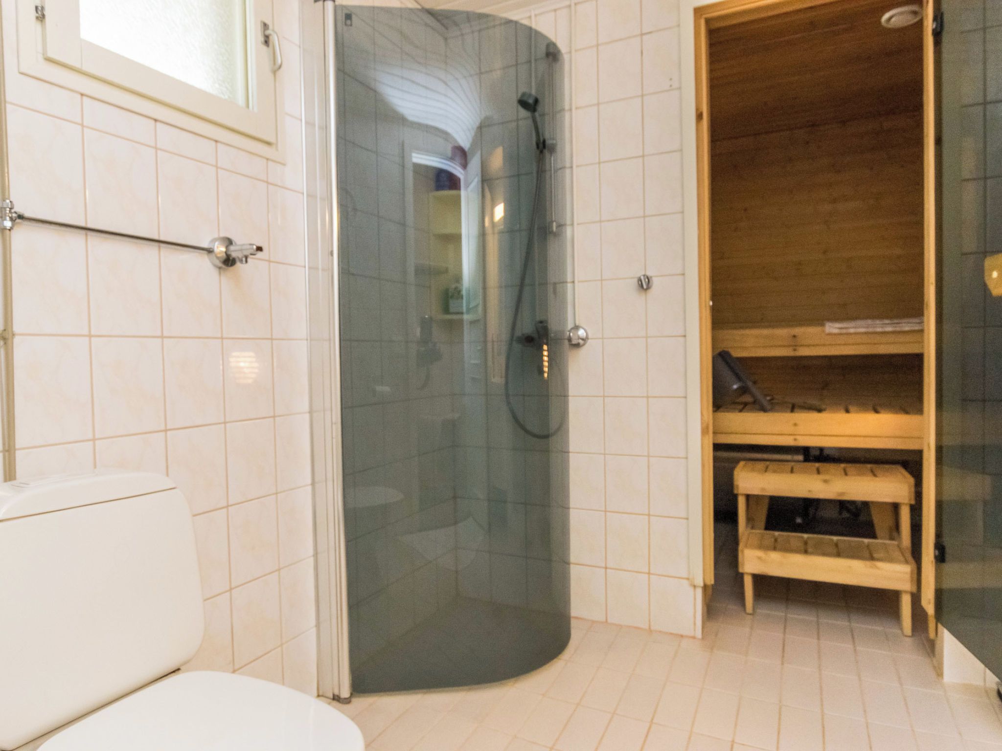 Kylpyhuoneessa on lasiseinäinen suihkukaappi, wc ja puinen penkki.