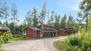 A gravel driveway leading to a row of red brick buildings with attached garages, surrounded by tall trees and greenery.