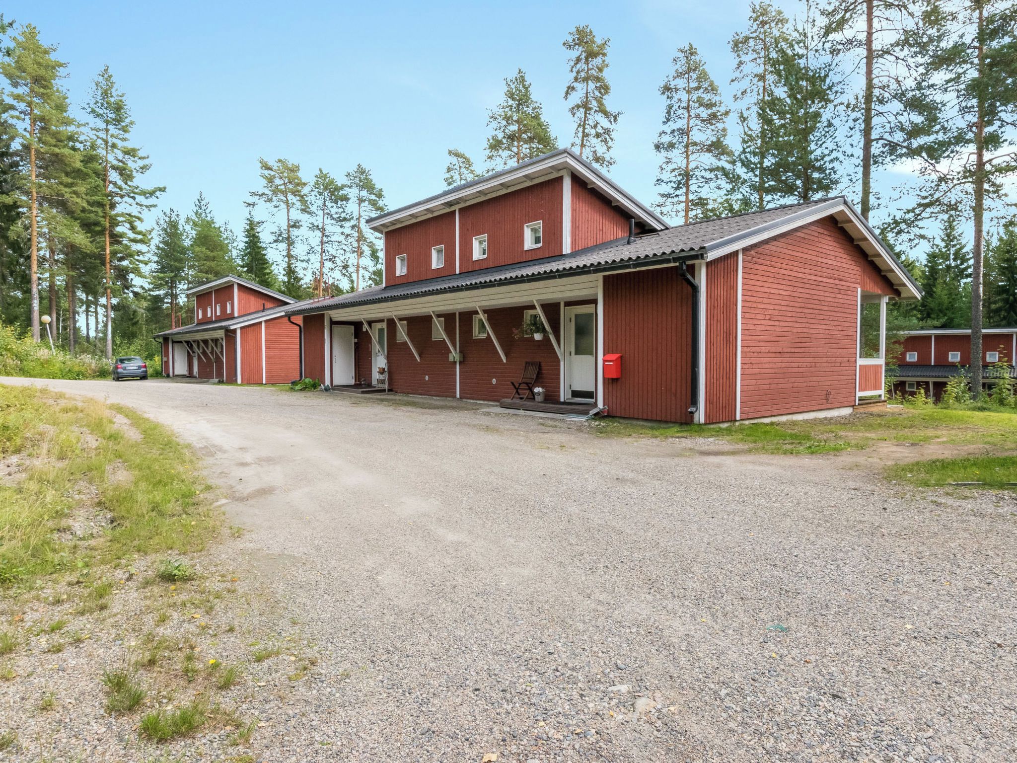 Punainen rakennus, jonka edessä on sorapäällysteinen ajotie ja katettu kuisti.