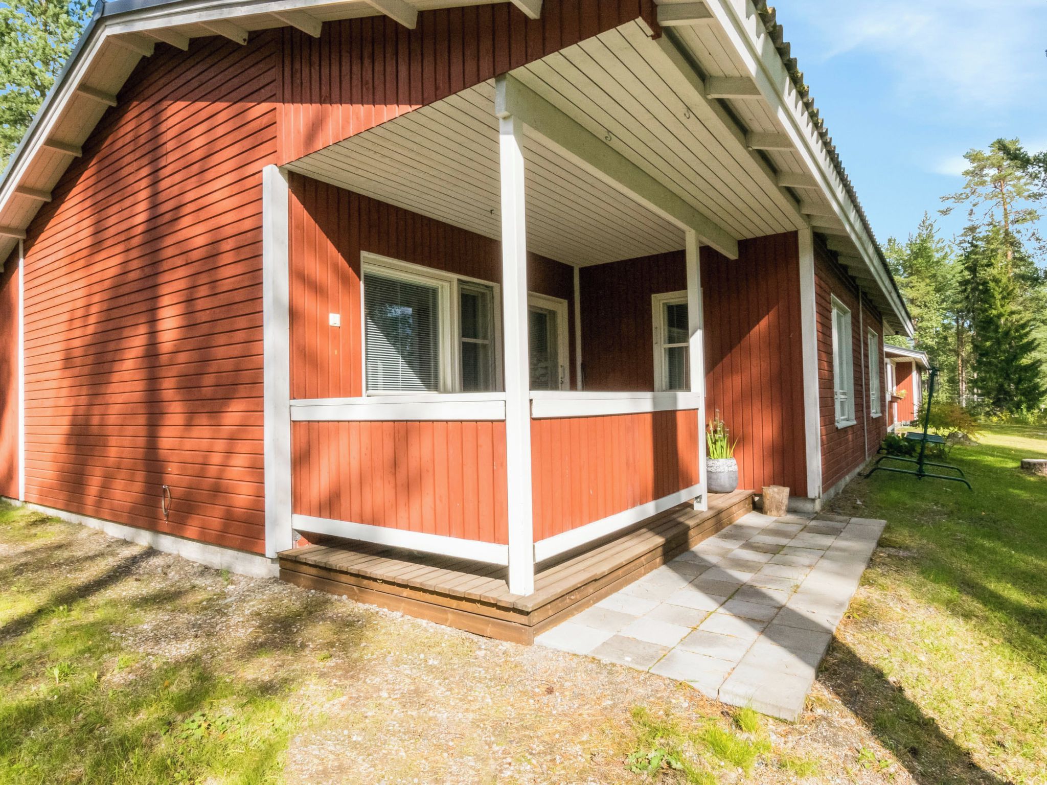 A red wooden house with a porch, a small front yard, and a visible garage.