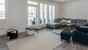A spacious living room with a grey sectional sofa, a coffee table, and a blue armchair. There are large windows with a view of the outdoors. - Villa elisabet by Interhome (Ristiina)