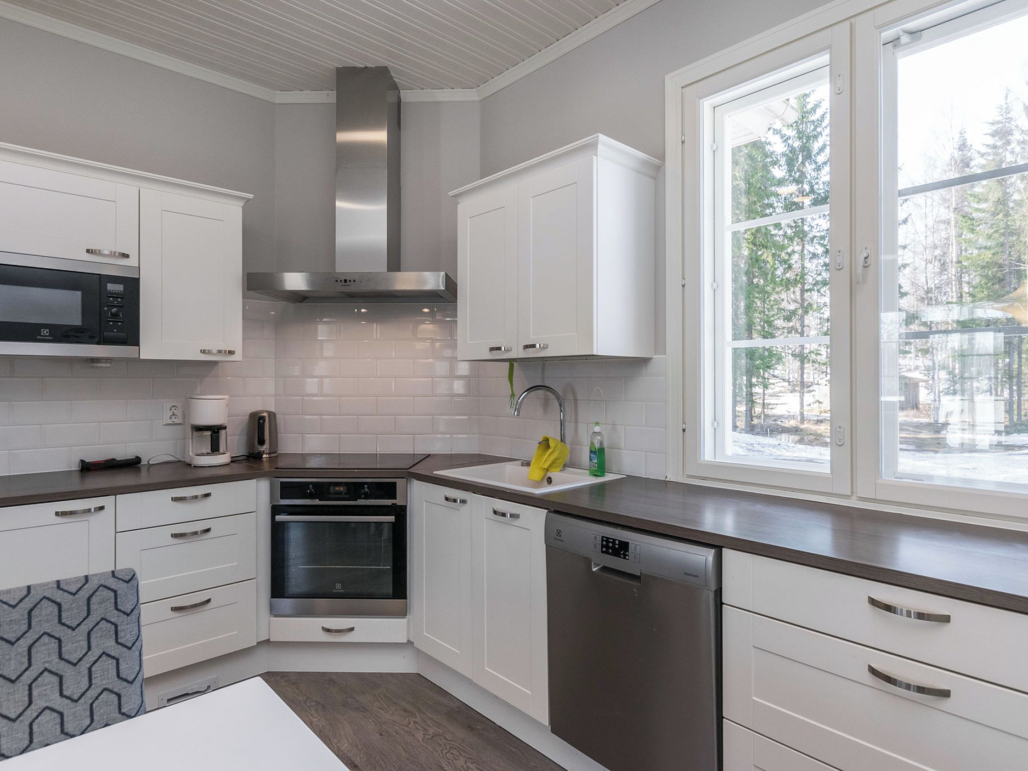 A modern kitchen with white cabinetry, stainless steel appliances, and a window providing a view of trees.