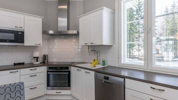 A modern kitchen with white cabinetry, stainless steel appliances, and a window providing a view of trees.