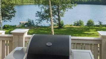 A grill on a deck overlooking a lake with trees and a dock in the background.