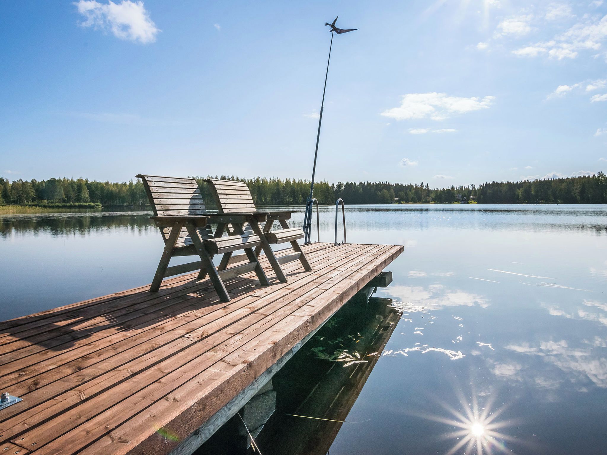 A wooden pier extending into calm water with a bench and a fishing rod.