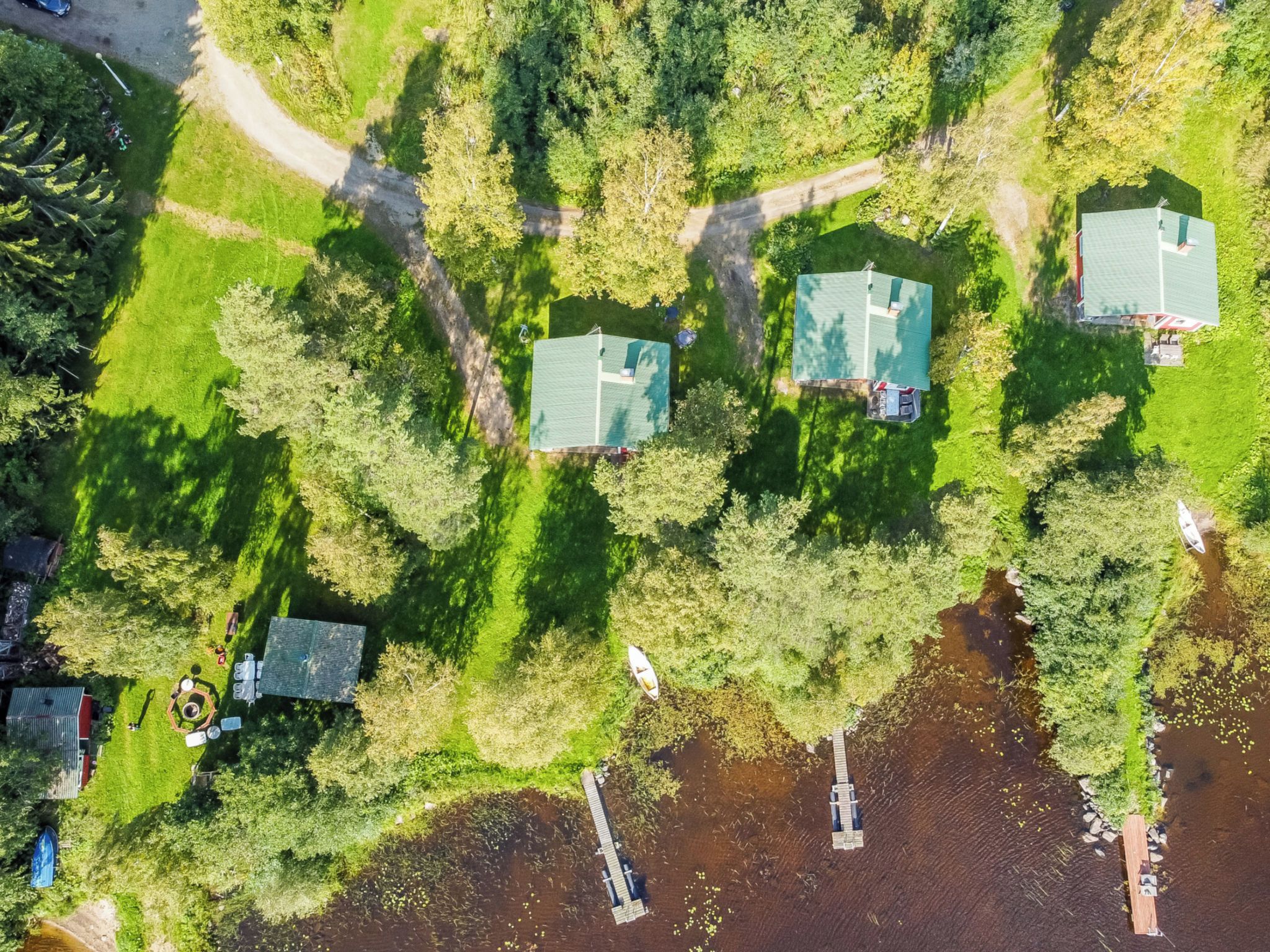 Vue aérienne d’un quartier r ésidentiel avec trois maisons, un quai et un petit bateau.