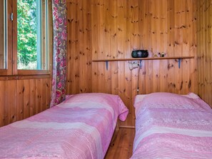 Ett rum med träväggar, två sängar med rosa sängkläder, en radio på en hylla och ett fönster med gardiner.