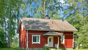 Una casa de madera roja con techo de tejas, una puerta blanca y un pequeño porche.