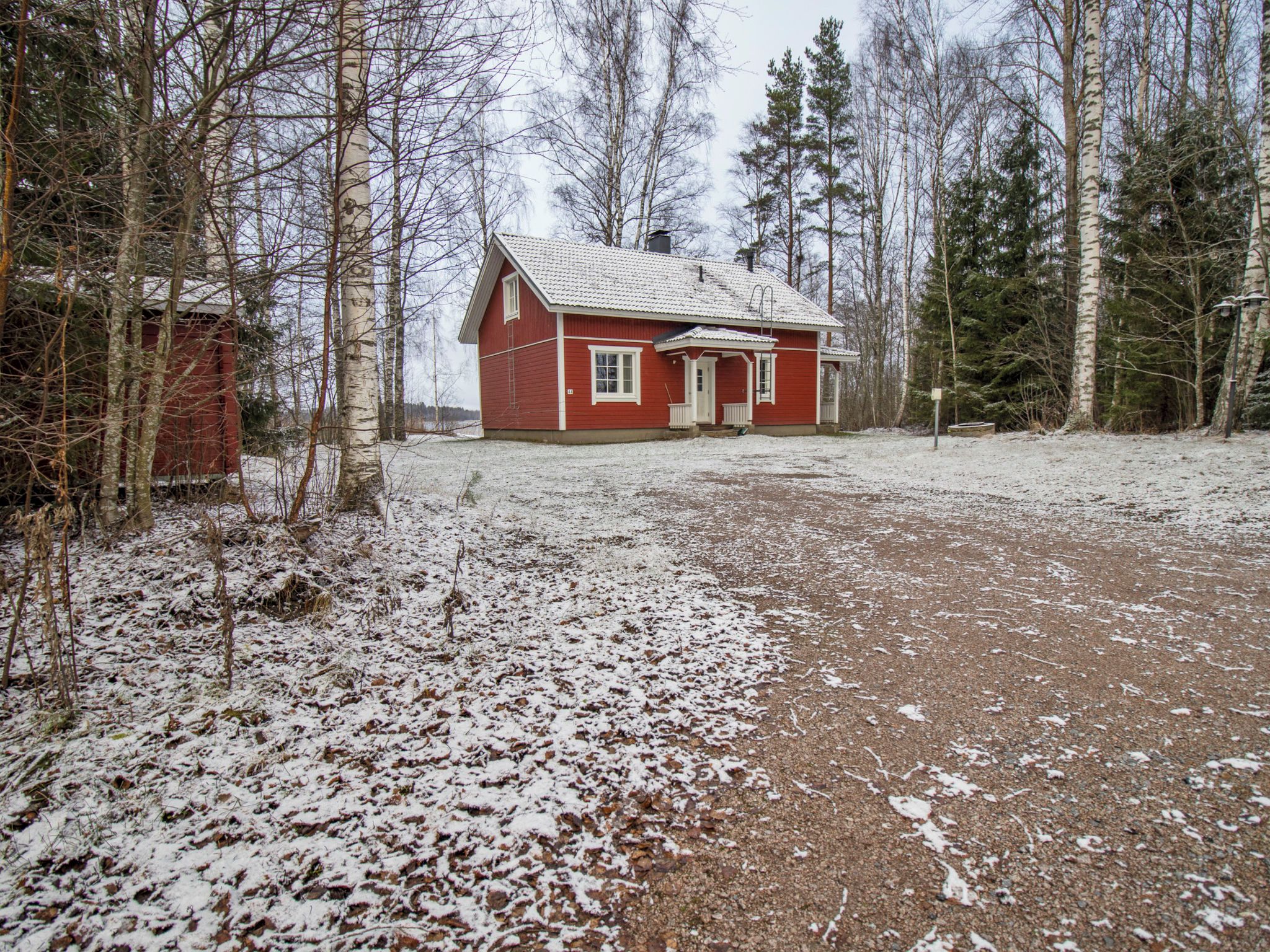 En röd trästuga med snötäckt mark och en skog i bakgrunden.