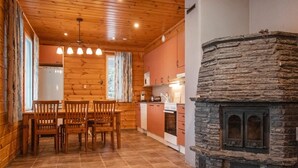 Un interior cálido de cabaña con chimenea de piedra, una mesa de comedor de madera y una zona de cocina.