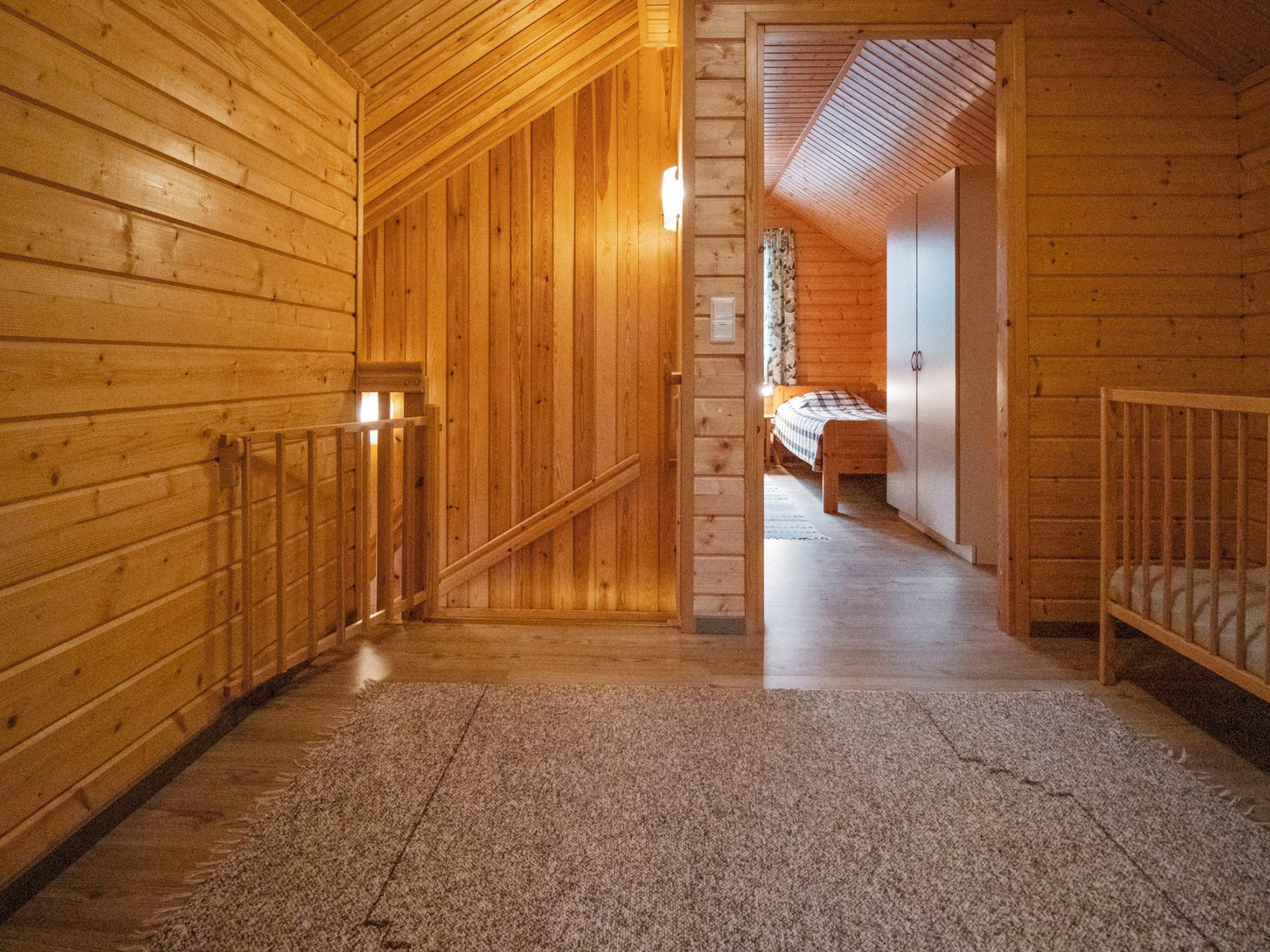 A wooden interior hallway leading to a bedroom with a bed and a crib.
