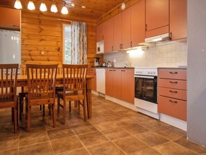 A kitchen with wooden cabinets, a stove, and a dining area with chairs.