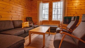 Un interior acogedor de cabaña de madera con suelo de madera, un sofá, una mesa y dos sillones.