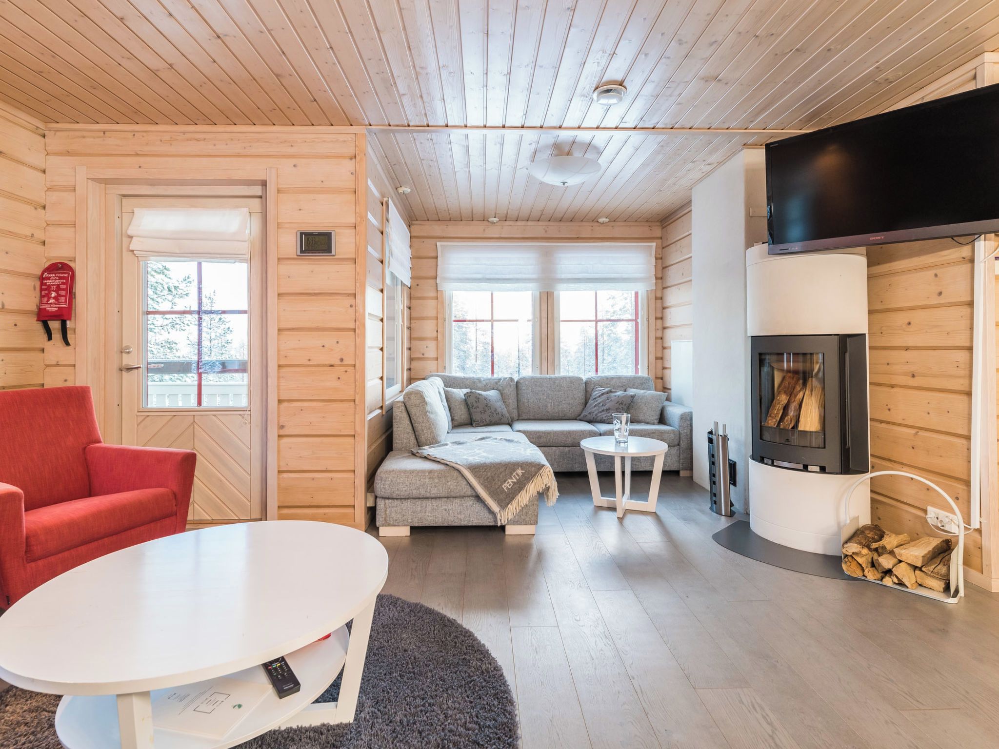 A cozy cabin interior with a sofa, red armchair, and a fireplace.