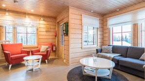 Interior acogedor de una cabaña de madera con un sillón rojo, un sofá gris y una mesa de centro blanca.