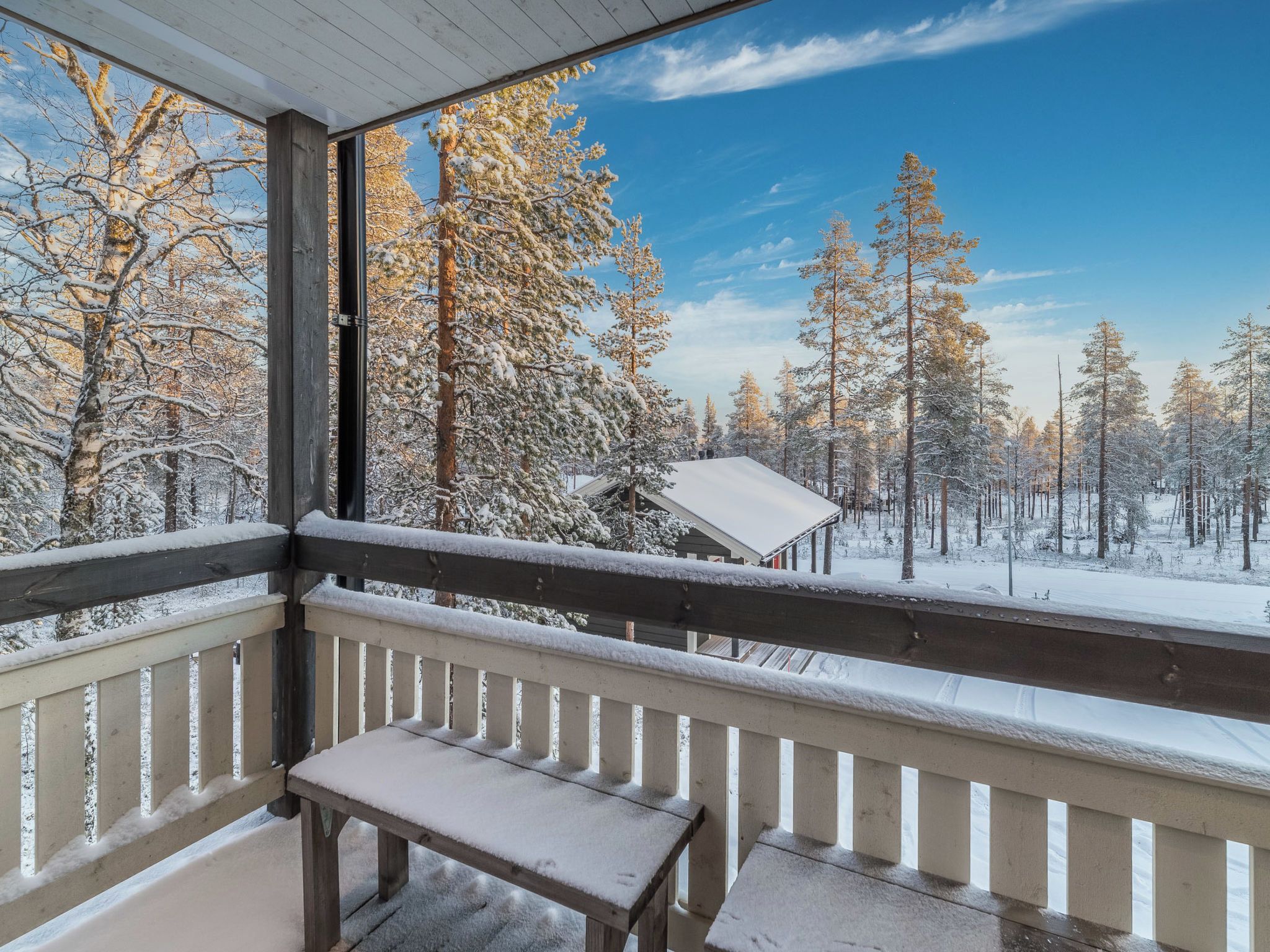Un balcon en bois avec un banc, donnant sur une forêt enneigée où s’élèvent de grands arbres.
